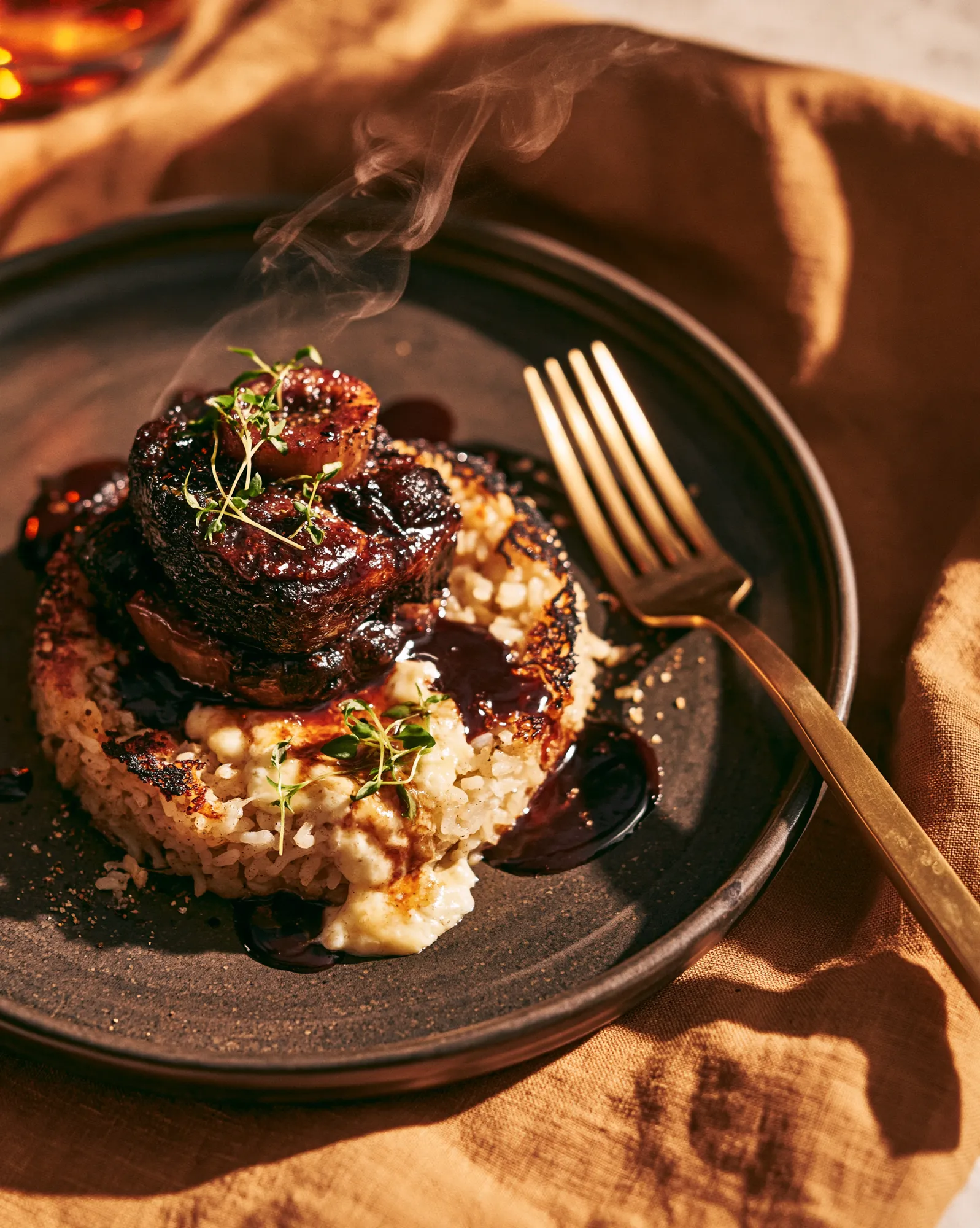 Oxtail over smoked jollof, steaming on a dark plate